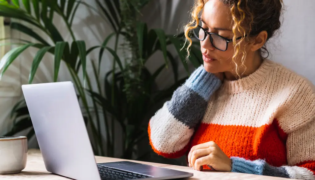 A woman at her laptop, resting her chin on her hand.