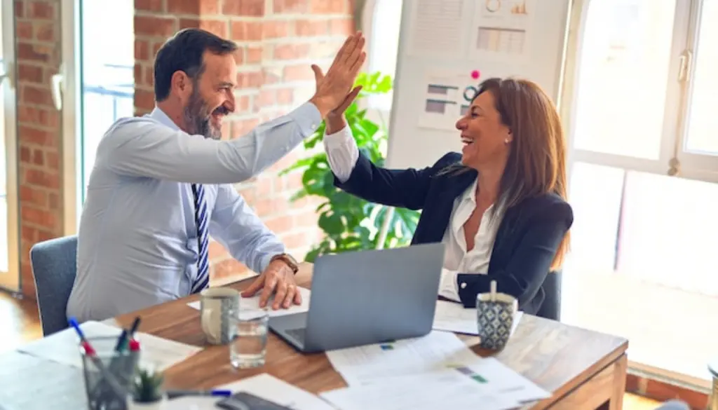 Two colleagues giving each other a high five across a desk.