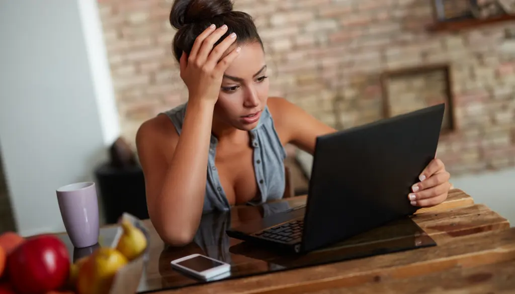 A woman frowning at her laptop, her head in her hand.