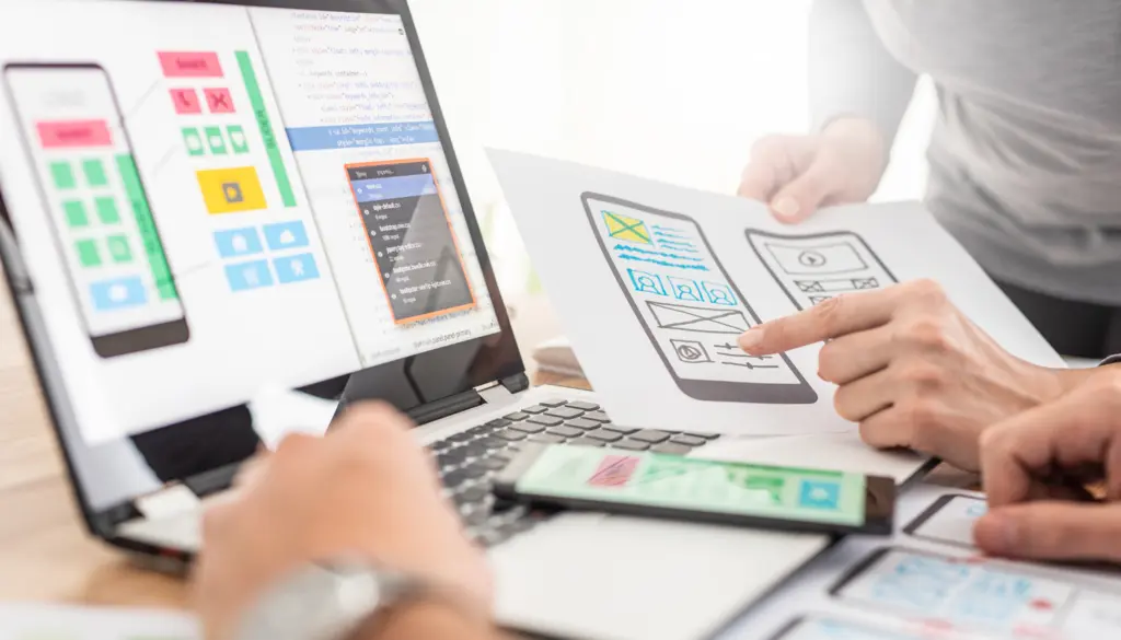 App screens and sketches on a laptop, a tablet and paper.