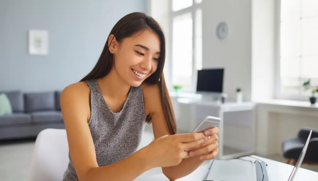 A woman smiling at her phone at home.