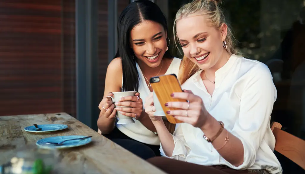 Two women laughing over a phone.