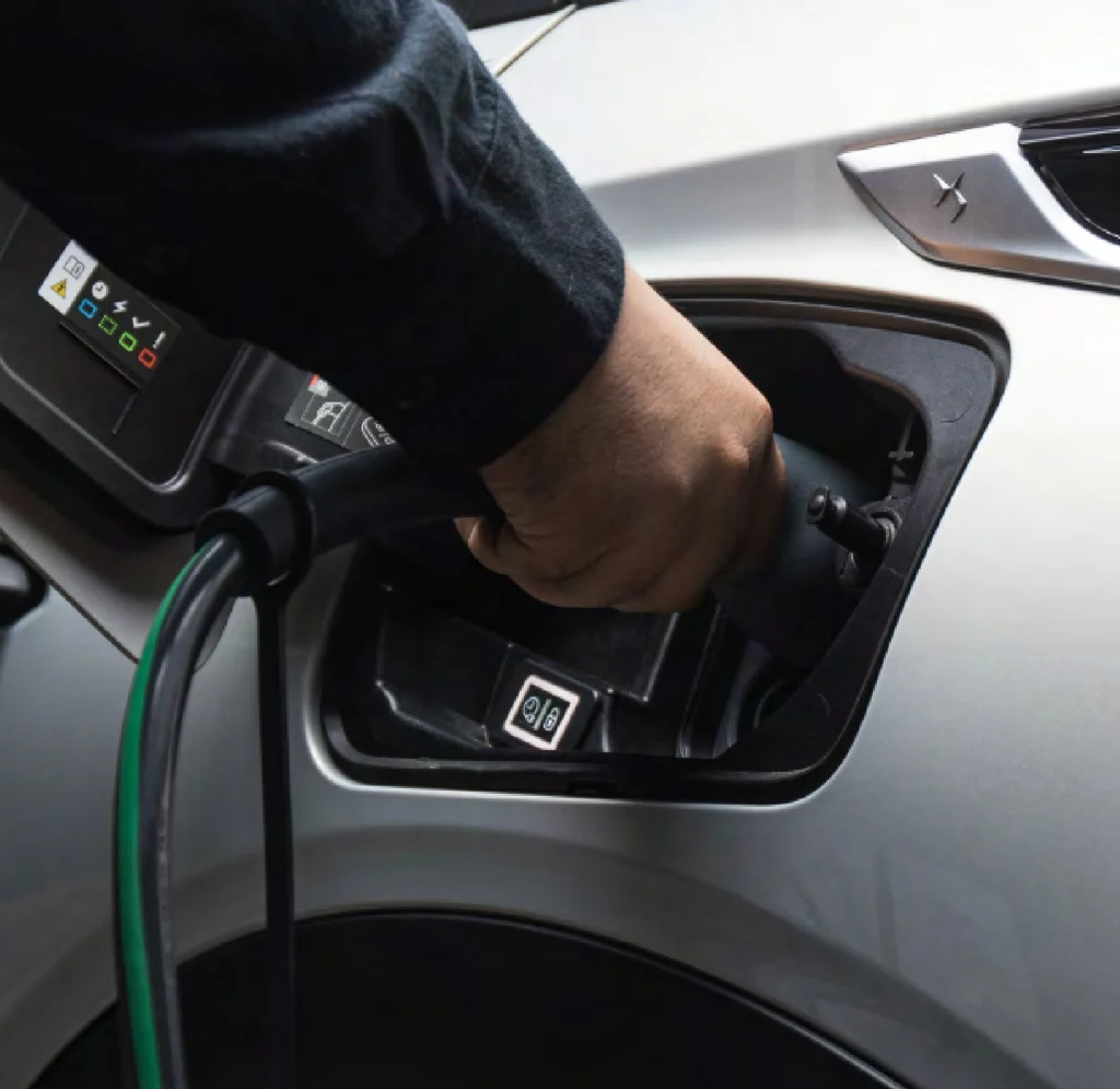 A hand plugging a charging cable into a silver car.