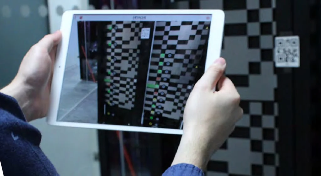 Someone holding a tablet up to a server rack, with the rack on its screen and a QR code on the rack to the right.
